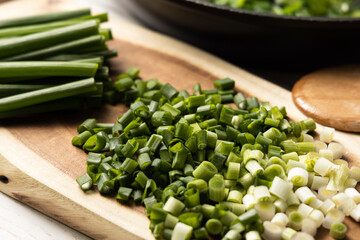 ​​Green onions cut on a wooden board. In the background a black pan.