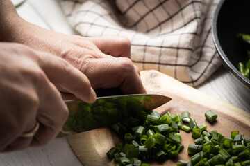 A man with a knife on a wooden board cuts ​​green onions.