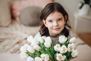 A girl in a white T-shirt with a bouquet of flowers. A girl with a smile has white tulips.