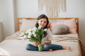 A girl in a white T-shirt with a bouquet of flowers. A girl with a smile has white tulips.