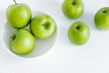 top view of green apples in bowl on white.