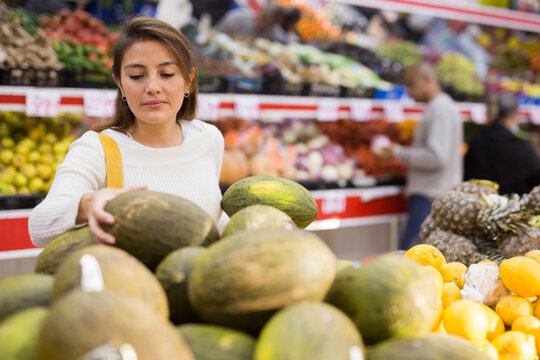 Positive woman picking ripe melon at grocery supermarket
