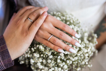 wedding rings on the hands of the newlyweds on the background of a bouquet