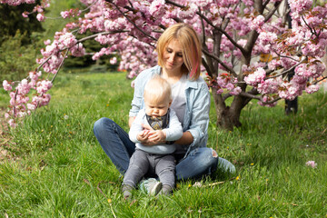Naklejka na ściany i meble Tender happy mother in a blue shirt sitting with a baby son in spring. Motherhood and femininity