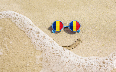 Sunglasses with flag of Romania on a sandy beach. Nearby is a sea lightning and a painted smile. The concept of a successful vacation in the resorts of Romania.