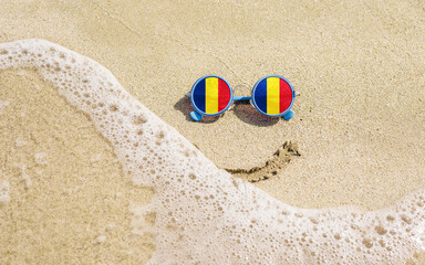 Obraz premium Sunglasses with flag of Romania on a sandy beach. Nearby is a sea lightning and a painted smile. The concept of a successful vacation in the resorts of Romania.