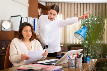 Irritated woman boss scolding stressed manager for incompetence with documents in office