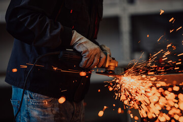 Heavy Industry Engineering Factory Interior with Industrial Worker Using Angle Grinder and Cutting a Metal Tube. Contractor in Safety Uniform and Hard Hat Manufacturing Metal Structures.