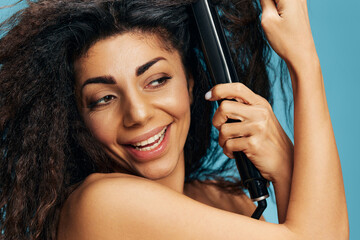Closeup portrait of overjoyed Latin curly woman using hair straightener, looking aside, posing...