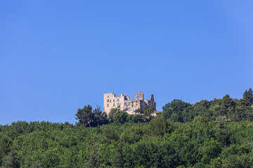 Fototapeta na wymiar Intimidating ruins of Lacoste castle, also known as castle of Marquis de Sade, on hill among dense foliage of surrounding forest against clear blue sky. Vaucluse, Provence, France