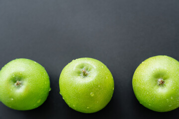 top view of green and fresh apples with water drops on black.