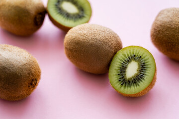 close up view of sweet whole and cut kiwi on pink.