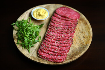 Salami slices with black pepper on a wooden board.