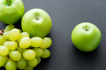 top view of tasty apples near green grapes on black.