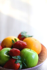 Pink bowl filled with fresh apples, oranges and strawberries on wooden table. Selective focus.