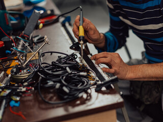 Industrial worker man soldering cables of manufacturing equipment in a factory. Selective focus