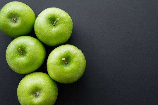 top view of whole and green apples on black.