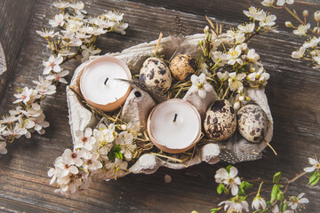 Candles in eggshells, quail eggs and white blossoming apple tree branches on a wooden tray as an Easter decoration