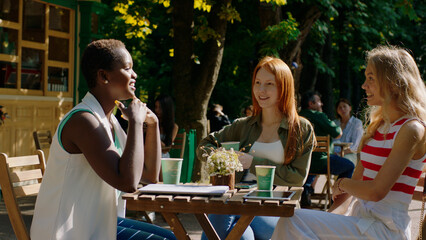Multiracial friends ladies very charismatic have a discussion in the middle of park they take a sit at coffee shop and enjoy the time together