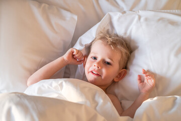 Obraz na płótnie Canvas Pretty toddler boy just woke up and basking in bed.