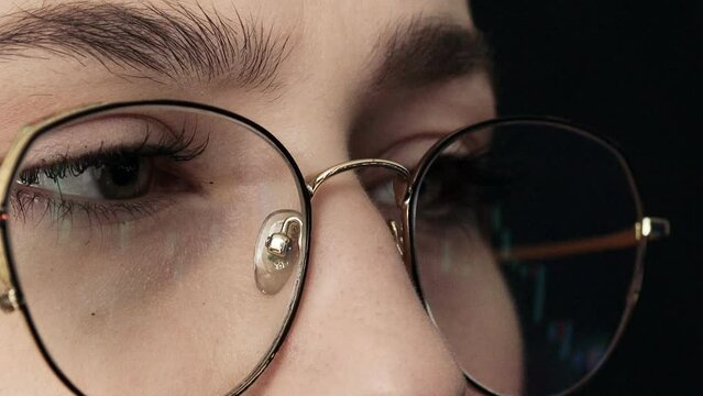 Close up of young woman's face and computer graphing display with glasses. Woman checking Bitcoin price chart on digital exchange on laptop, cryptocurrency future price action prediction