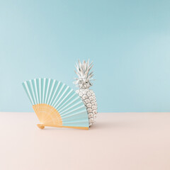 White pineapple with blue paper fan on blue and pink background. Minimal summer concept idea.