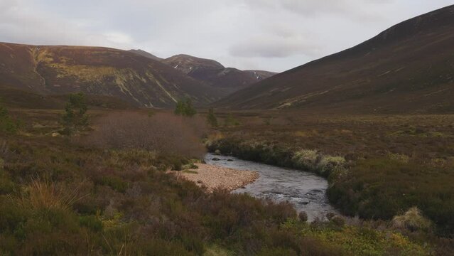 A scenic still footage of a mountain river winding accross moorland with a Scottish mountain valley and summit in the background under a stormy grey sky
