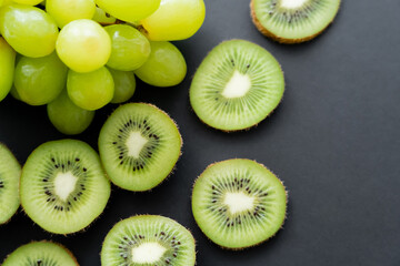 top view of green grapes and sliced kiwi on black.
