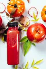 Red smoothie drink in bottle surrounded by red apples, tomatoes and beets