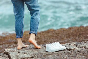 woman walking barefoot by seaside holding hands white shoes. summer vacation