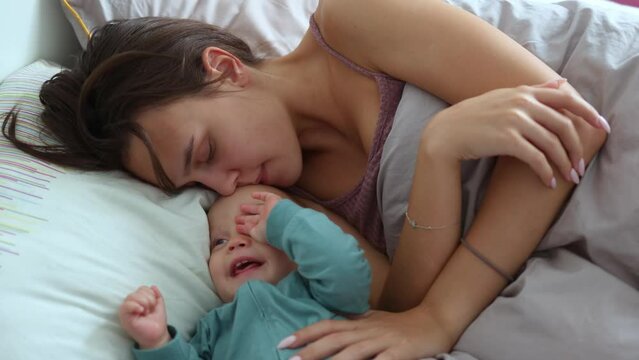 young mother and her infant baby having fun playing in bed morning. mom and baby child together spending time cuddling in bedroom waking up. 