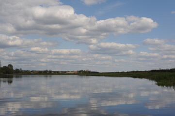 Picturesque and peaceful cloudscape with white clouds and blue sky reflecting in the river in spring or summer in Poland