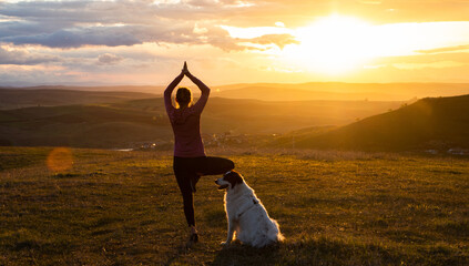 woman with white dog doing yoga at sunset tree pose  vrksasana