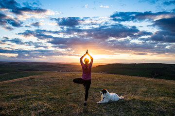 woman with white dog doing yoga at sunset tree pose  vrksasana