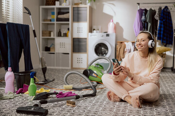 Woman in sweatpants sits on floor uses cell phone listens to music on wireless headphones, changes playlist on app, cleans laundry room, bathroom.