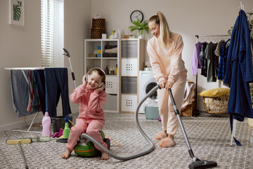 Woman cleans bathroom laundry room vacuums floor with vacuum cleaner. On equipment sits girl who...