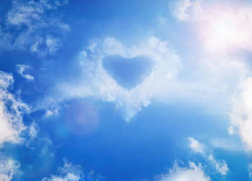 Blue sky with white fluffy clouds in form of a heart with sun on sky, soft focus. Clouds look like a heart. Love, lover, imagination, Valentine's Day, Women's Day, Mother's Day concept. Copy space.