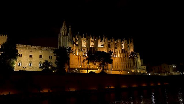 Night static shot of the Cathedral of Palma de Mallorca (La Seu) with people walking along the pond - Spain