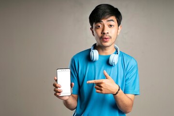 handsome boy wearing a blue t-shirt and using headphones pointing at his cellphone