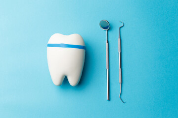 The concept of oral health. Tooth, diagnostic bilateral periodontal probe and diagnostic dental mirror made of stainless steel. Dental equipment is highlighted on a blue background in close-up.