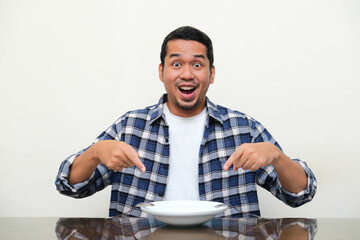 Adult Asian man pointing to empty plate with wow face expression
