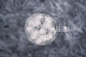 drinking enough water or sobriety concept, pint glass with tap water and ice cubes over grey concrete