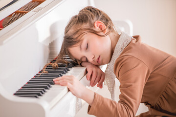 A little girl fell asleep on the keyboard on a large white piano in a bright sunny room