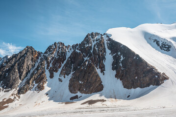 Scenic mountain landscape with glacier under sharp rocks in sunlight. Awesome alpine landscape with glacial tongue in sunshine. Beautiful view to snow mountain tops at very high altitude in sunny day.