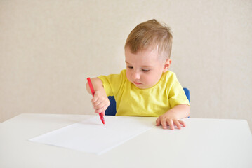 toddler boy plays draws on a piece of paper with a red pen sitting at a white table. educational game Montessori fine motor skills. early development concept.