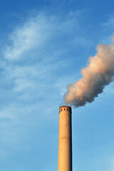 Smoke billowing out the tall chimeny of a power station at dusk isolated against a blue sky. No people. Copy space.