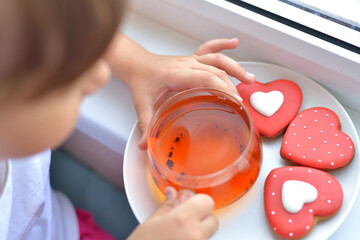A girl in a white T-shirt holds a cup of tea and a liver in the form of a red heart. delicious sweet snack concept.
