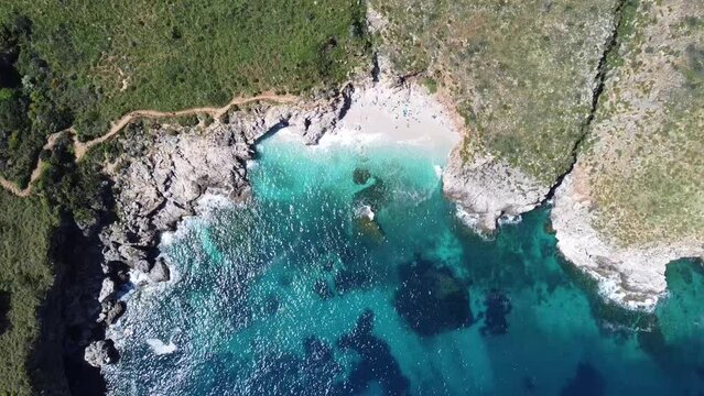 imposing green cliffs over a perfect little bay with white sand, near zingaro in sicily in italy, nice weather (droneshot)
