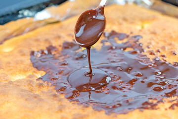 Melted chocolate flows from the spoon onto the cake.