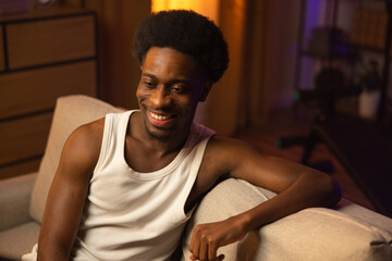 Happy laughing boy spends the afternoon watching a comedy movie, afro handsome muscular guy relaxes...